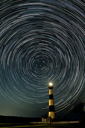 Star trails over Bodie Island Light Station and an airplane streaking diagonally across the sky.
