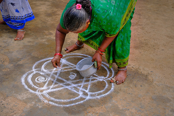 Indian woman demonstrates kolam, a traditional form of creating patterns with colored chalk.