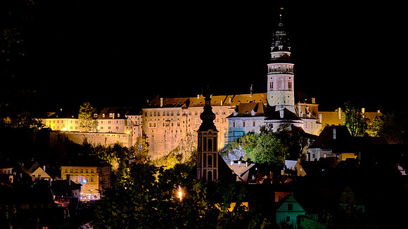 Český Krumlov village, castle, tower, and St. Jost church at night.